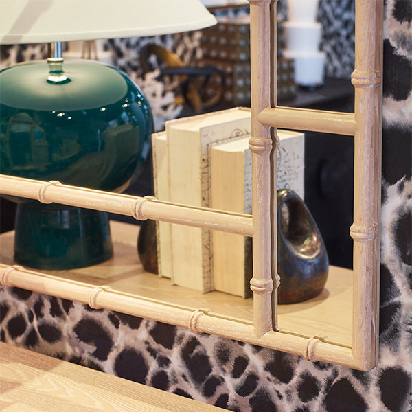 Decorative mirror with bamboo frame on a surface with books and a green lamp.