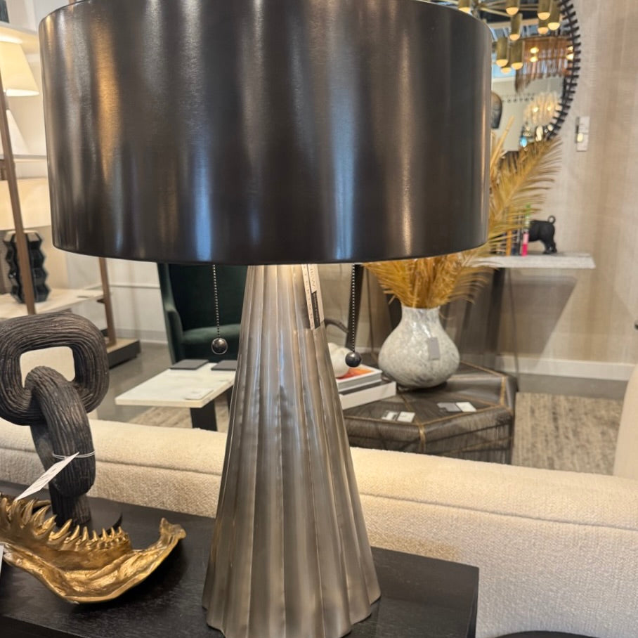 Decorative table lamp with a black shade and ribbed base on a dark surface.