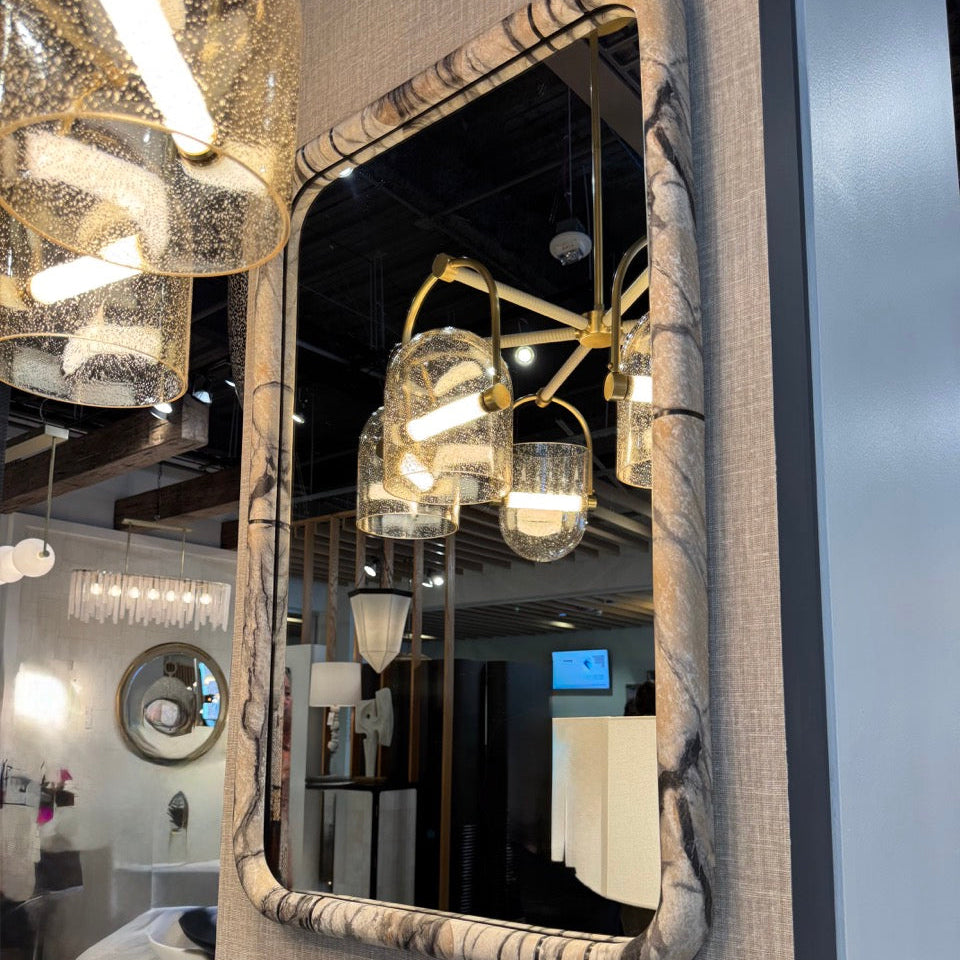 Decorative mirror with textured frame reflecting a room with modern lighting fixtures.