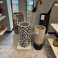Decorative cylindrical vases with patterned designs on a tiled floor.