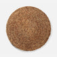 A round woven natural fiber placemat or rug in a warm tan-brown color, photographed from directly above on a light gray background.