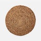 A round woven natural fiber placemat or rug in a light brown tan color, shown from a top-down view on a light gray background.
