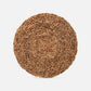 A round woven natural fiber placemat or rug with a textured, coiled basket-weave pattern in warm tan and brown tones, shown on a light gray background.