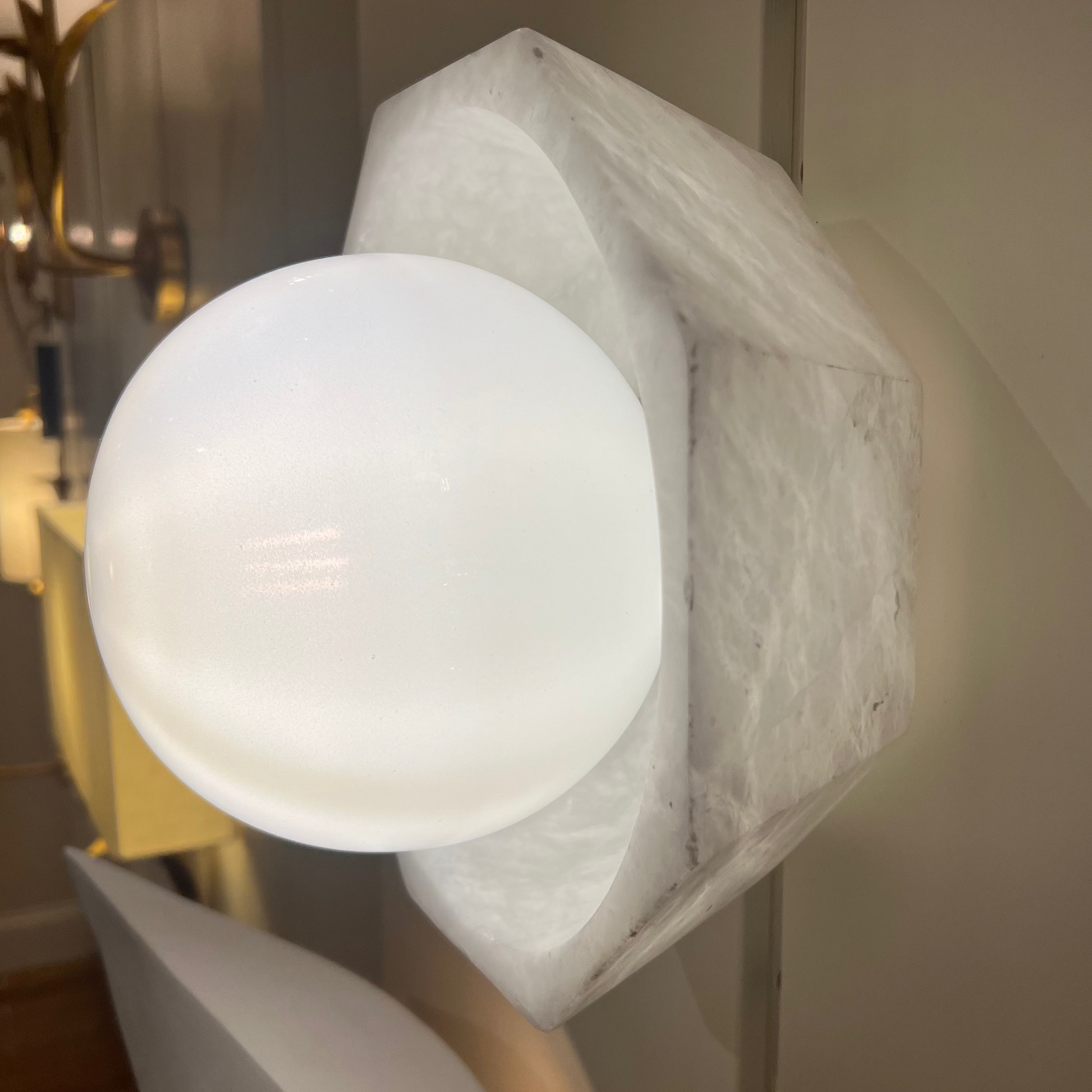 Modern wall-mounted light fixture with a spherical white bulb in a room setting.