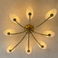 A mid-century modern ceiling light fixture with a brass-finished central hub and eight curved arms, each ending in a frosted oval glass shade. The fixture is shown illuminated against a textured off-white plaster ceiling.