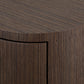 Close-up of a dark brown textured furniture piece with a curved top and vertical slatted front, showing a black drawer or panel inset.
