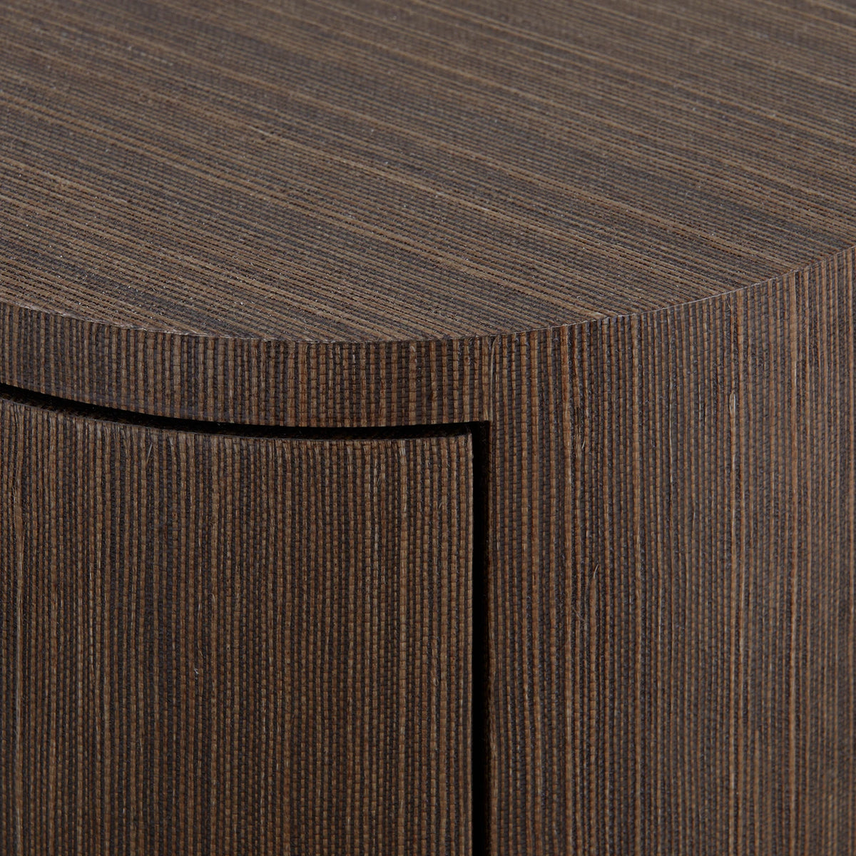 Close-up of a dark brown textured furniture piece with a curved top and vertical slatted front, showing a black drawer or panel inset.