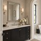 A modern bathroom vanity featuring a black double-sink cabinet with silver knobs, a white marble countertop, a large beaded silver mirror, and wall-mounted sconces.