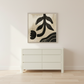 White dresser with abstract black and white artwork on a light beige wall.