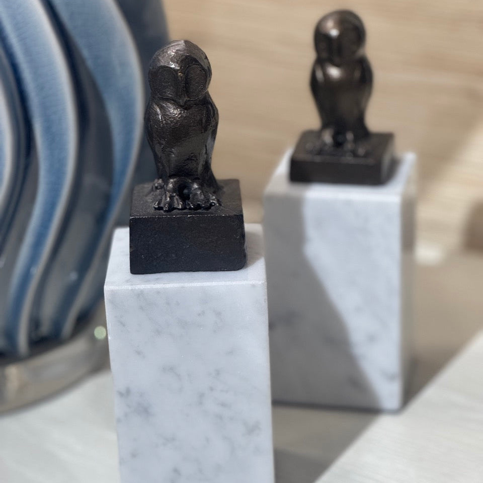 Two owl sculptures on marble bases with a blurred background