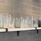 Set of clear glass tumblers on a shelf against a tiled wall.