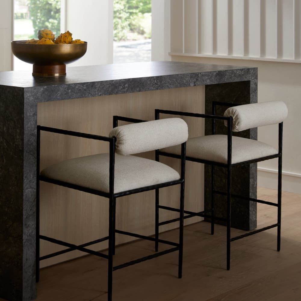 Three bar stools with white cushions in front of a marble countertop.