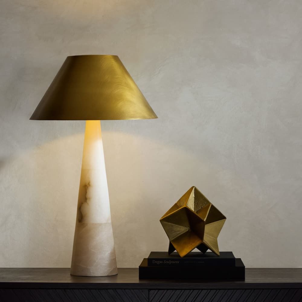 Decorative table lamp with a gold shade and marble base next to a geometric gold sculpture on a wooden surface.