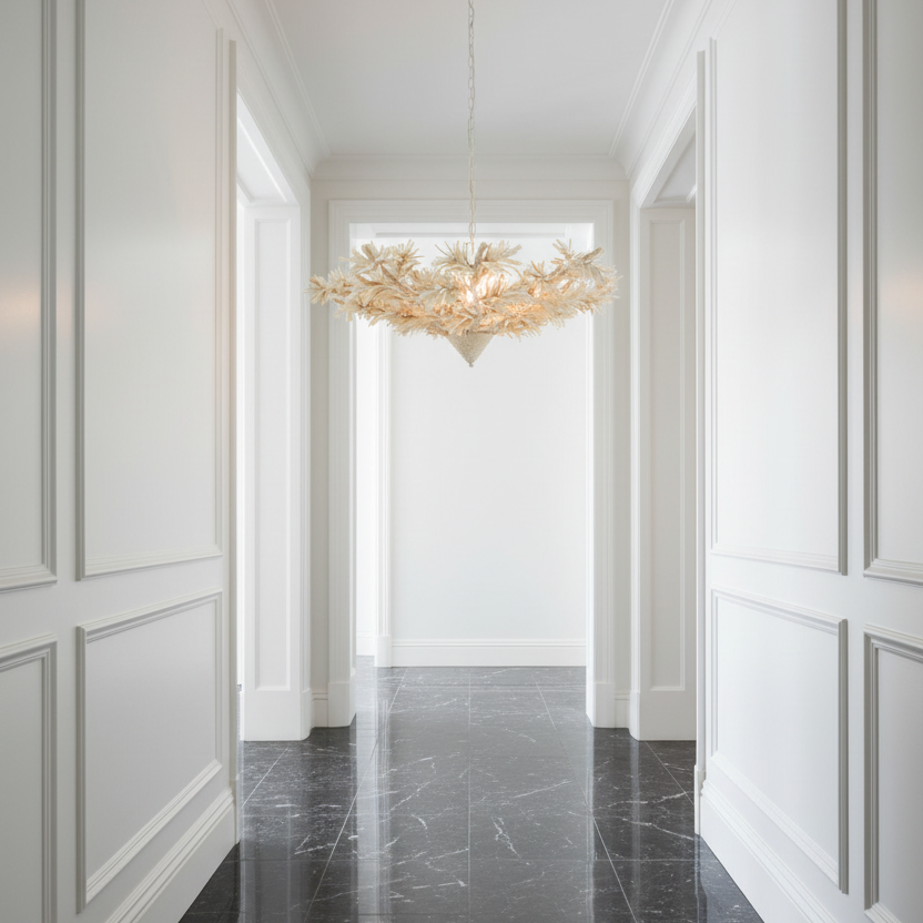 A modern chandelier with a branching, coral-like structure made of warm cream and gold-toned elements, hanging in a bright white hallway with paneled walls and a dark marble floor.
