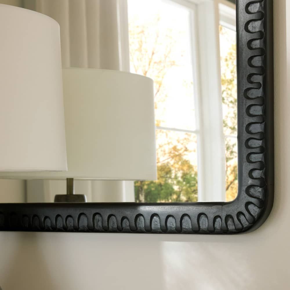 Decorative mirror with a textured black frame on a wall.