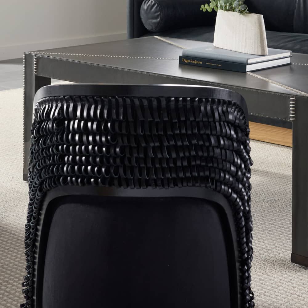Black woven stool in front of a modern coffee table with a plant and books.