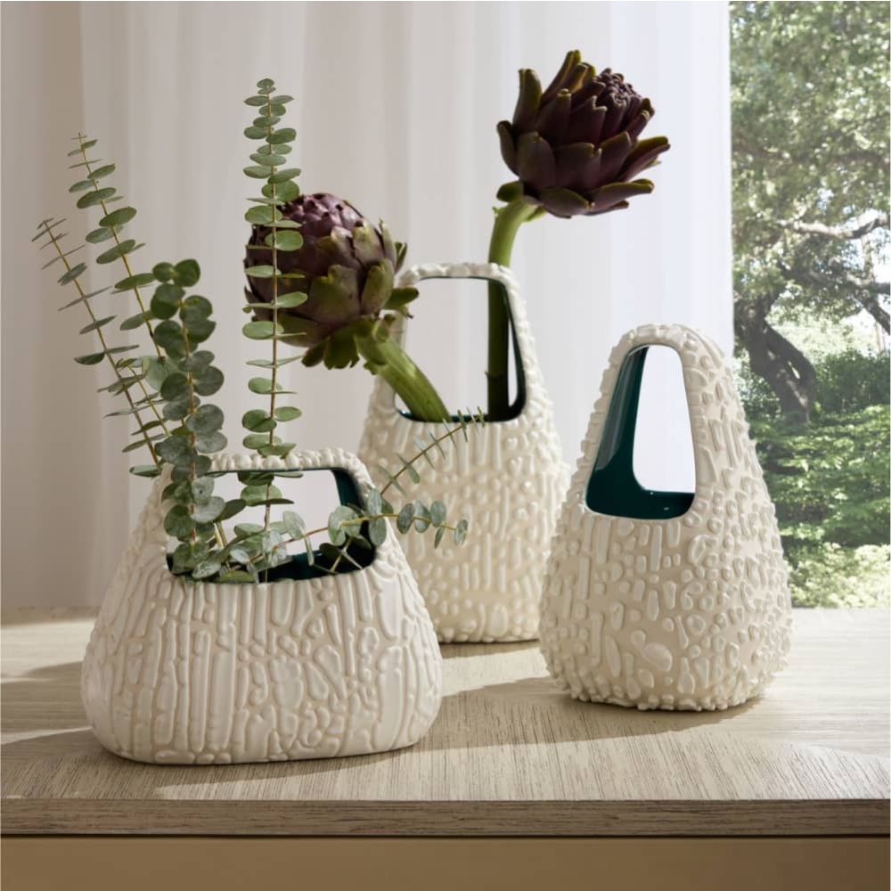 Set of three textured white vases with plants on a wooden surface