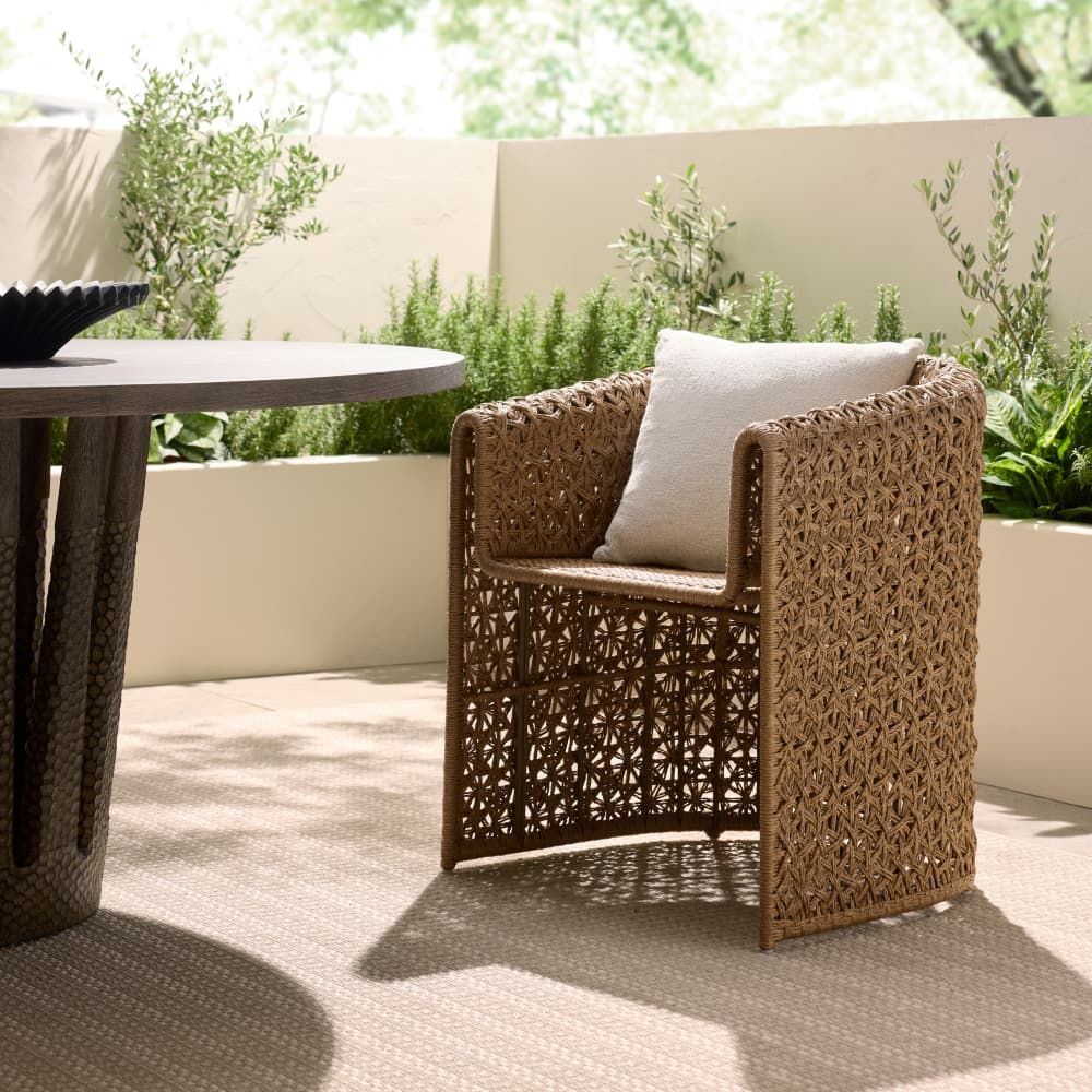 Wicker chair with a cushion on a patio with a table and plants in the background