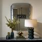 Decorative items including a lamp, mirror, and vases on a surface with a neutral background.