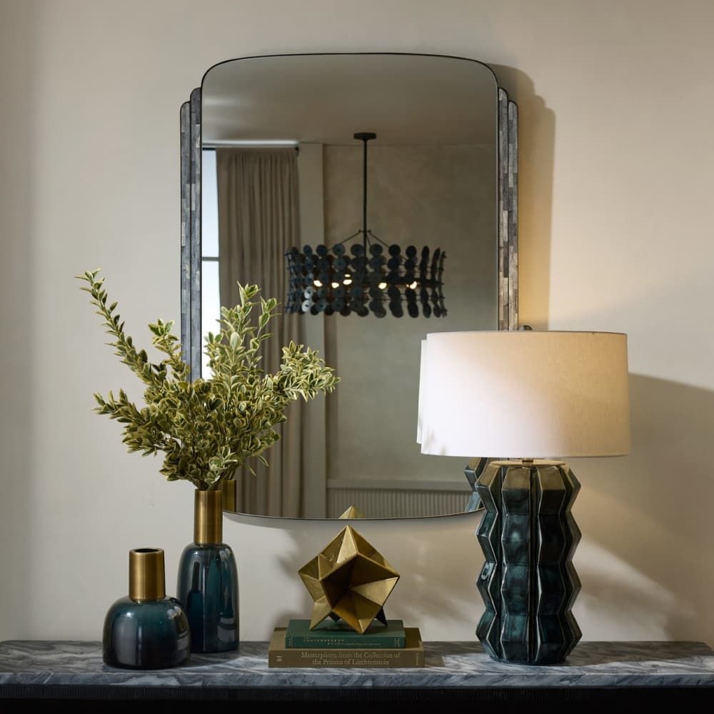 Decorative items including a lamp, mirror, and vases on a surface with a neutral background.