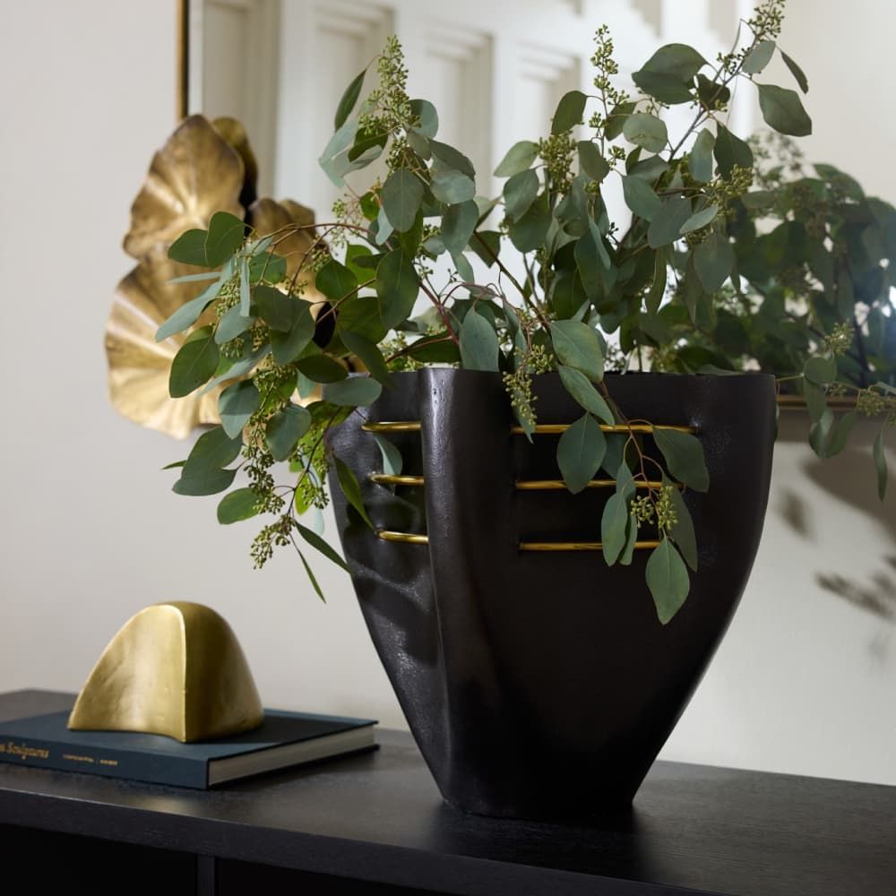 Decorative vase with green leaves on a table next to a gold sculpture and book.