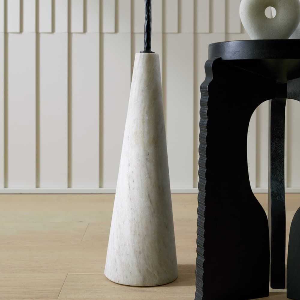 White marble vase and black decorative object on a wooden floor with a neutral wall background