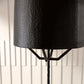 Close-up of a black textured lampshade on a white paneled wall background