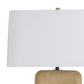 Table lamp with a white shade and textured beige base on a white background