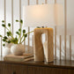 Decorative lamp with textured base on a wooden surface with books and a vase.