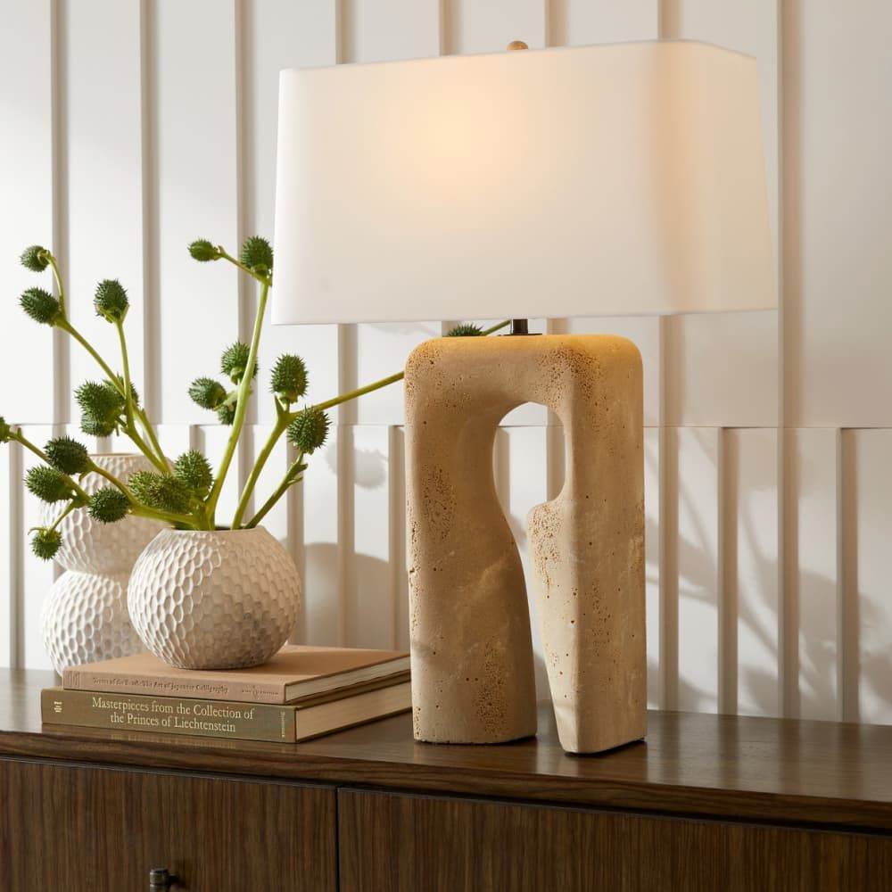Decorative lamp with textured base on a wooden surface with books and a vase.