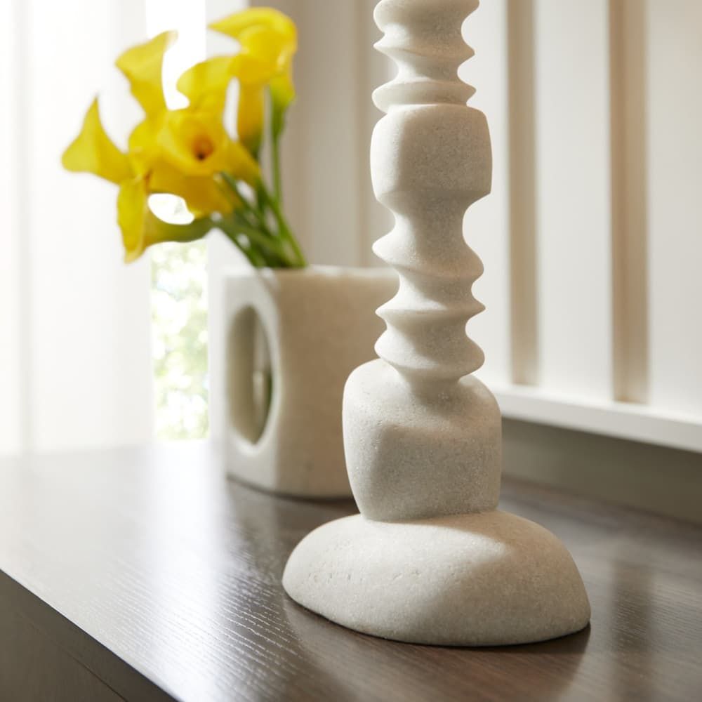Decorative white candlestick on a wooden surface with yellow flowers in the background