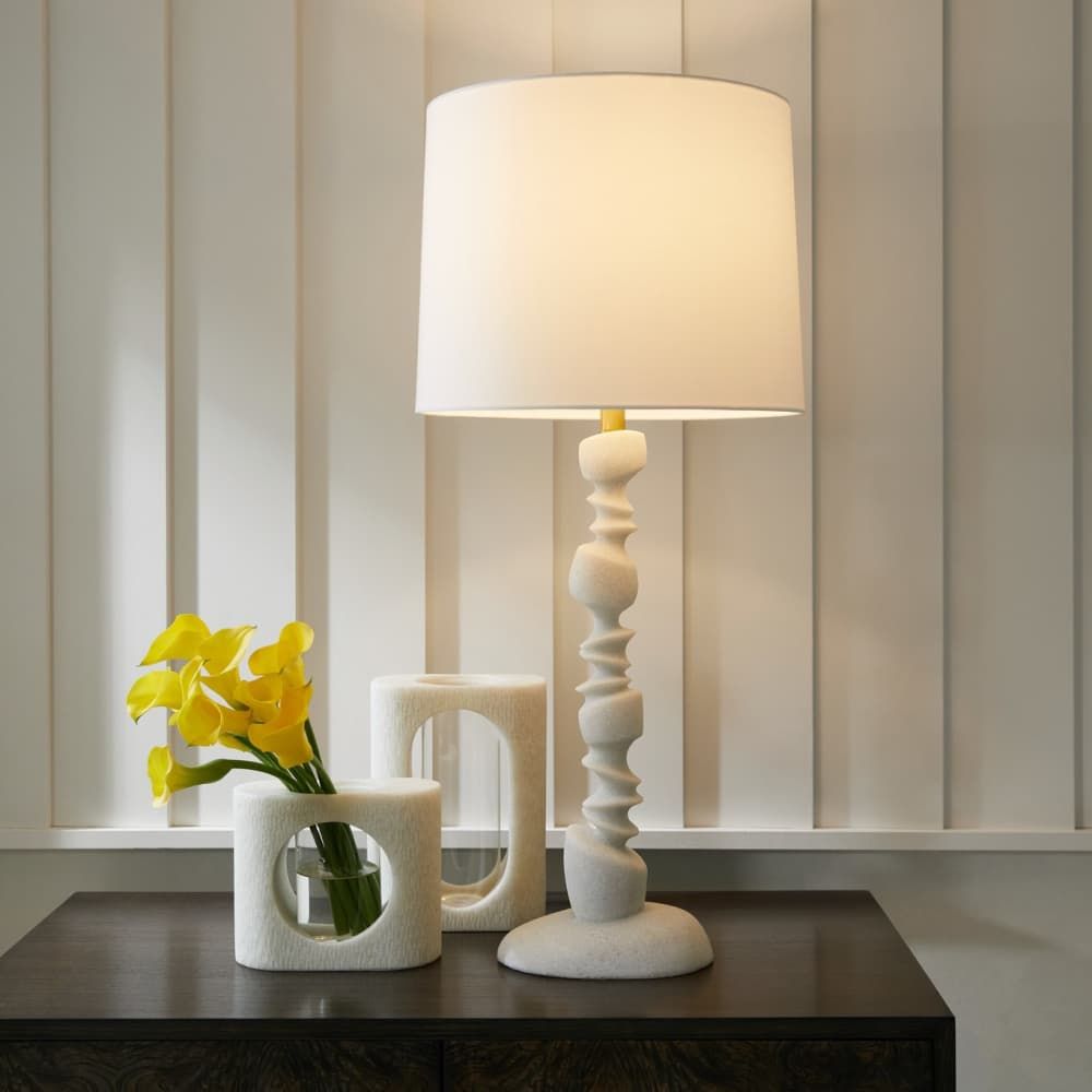 White table lamp and decorative vase with yellow flowers on a dark surface.