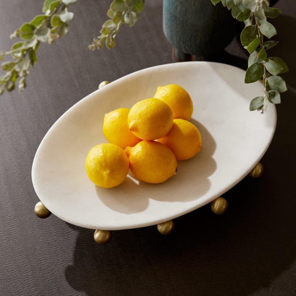 White oval plate with lemons on a dark surface with greenery