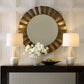 Decorative round mirror with a wooden frame on a wall above a console table with lamps and flowers.