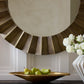Decorative mirror with a sunburst design above a table with pears and a vase of flowers.