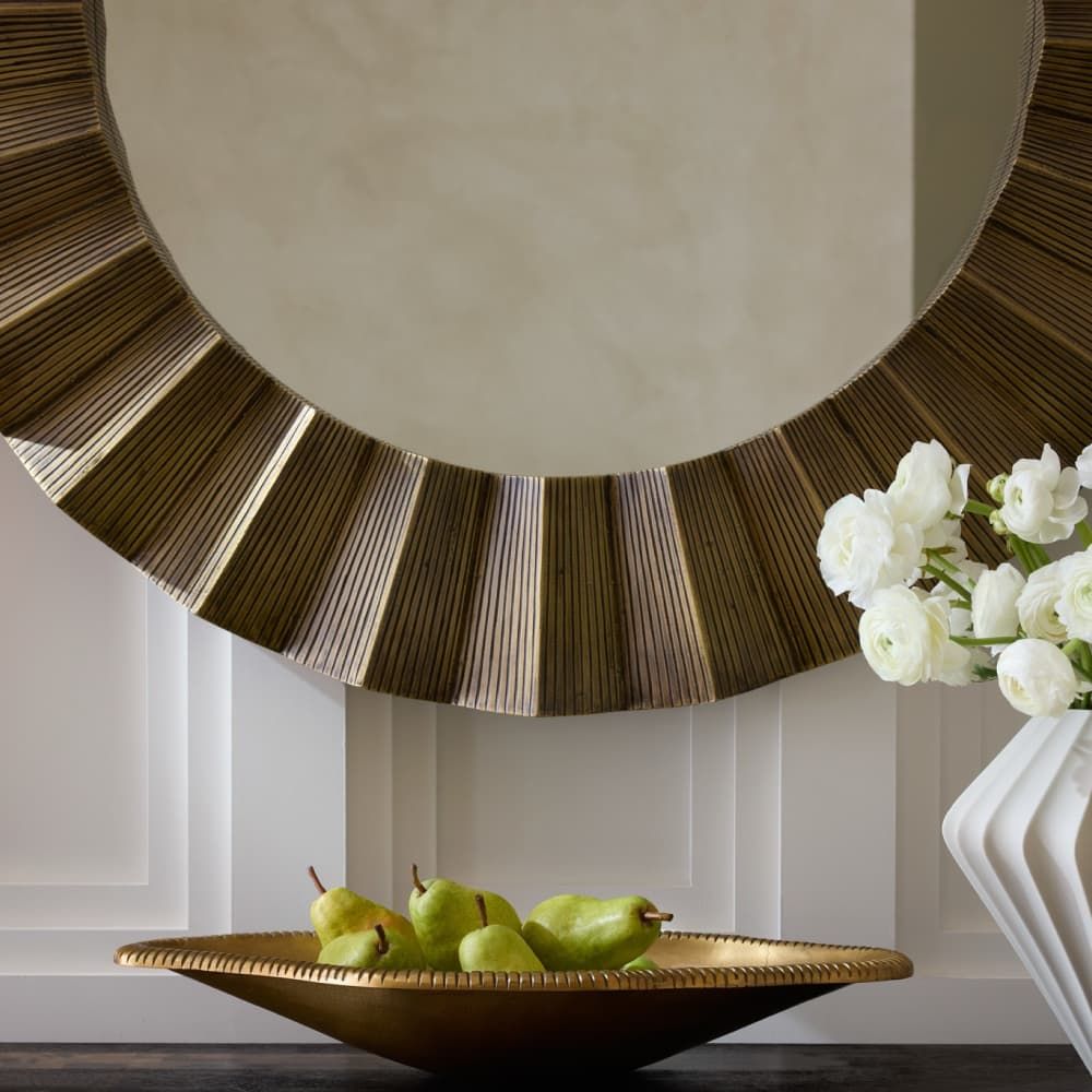 Decorative mirror with a sunburst design above a table with pears and a vase of flowers.