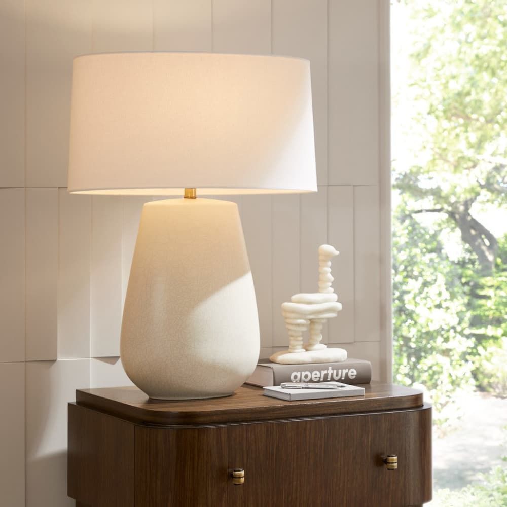Beige table lamp on a wooden side table with a blurred outdoor scene in the background