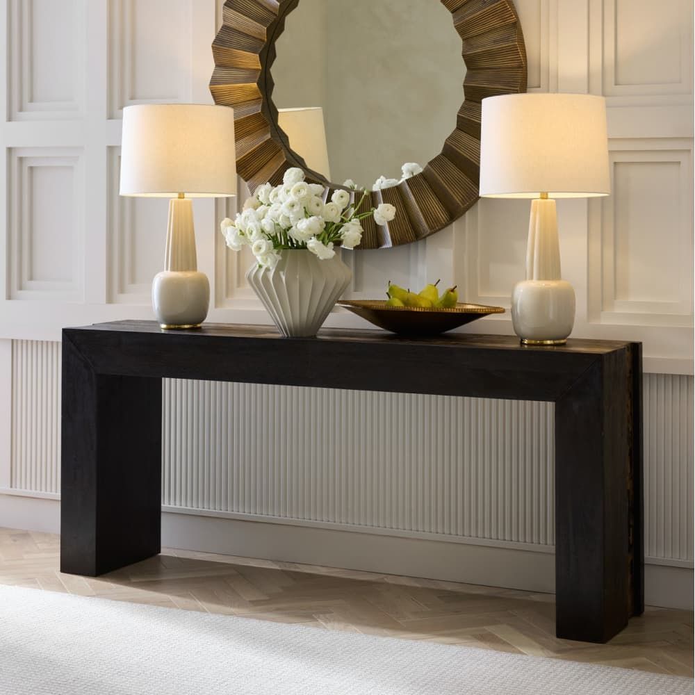 Console table with two lamps and a decorative mirror in a room setting.