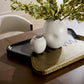 Two white ceramic vases on a dark wooden tray with a plant in the background.