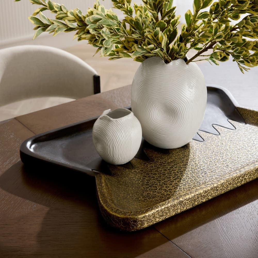 Two white ceramic vases on a dark wooden tray with a plant in the background.
