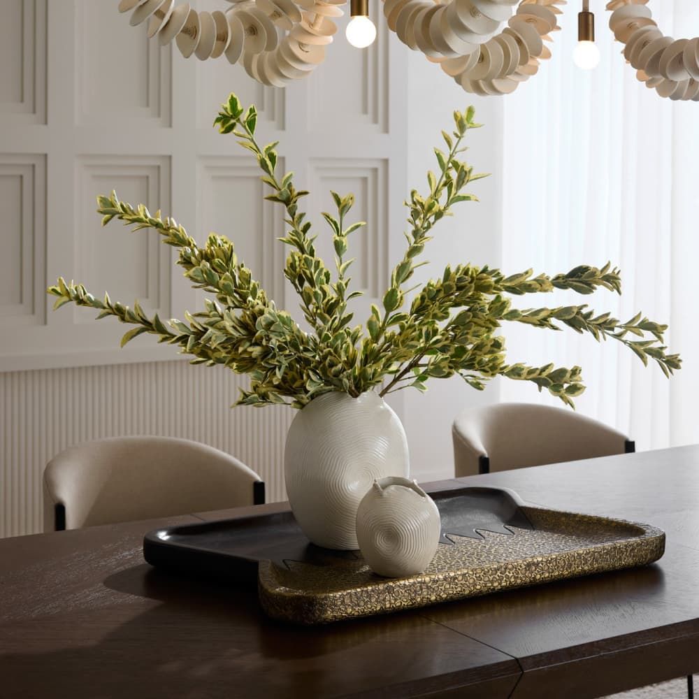 Decorative setting with a white vase, green plant, and black tray on a wooden table.