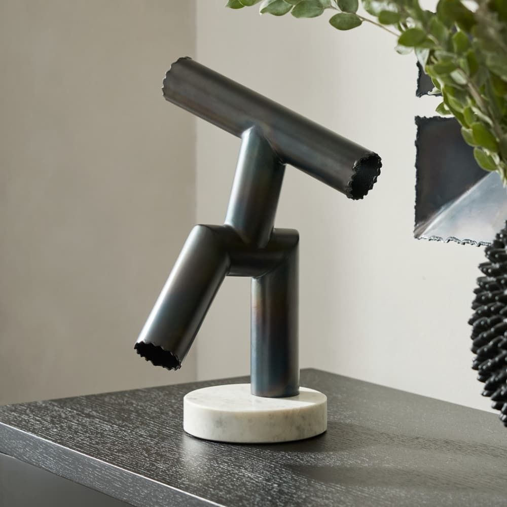 Modern black metal sculpture on a marble base with a plant in the background