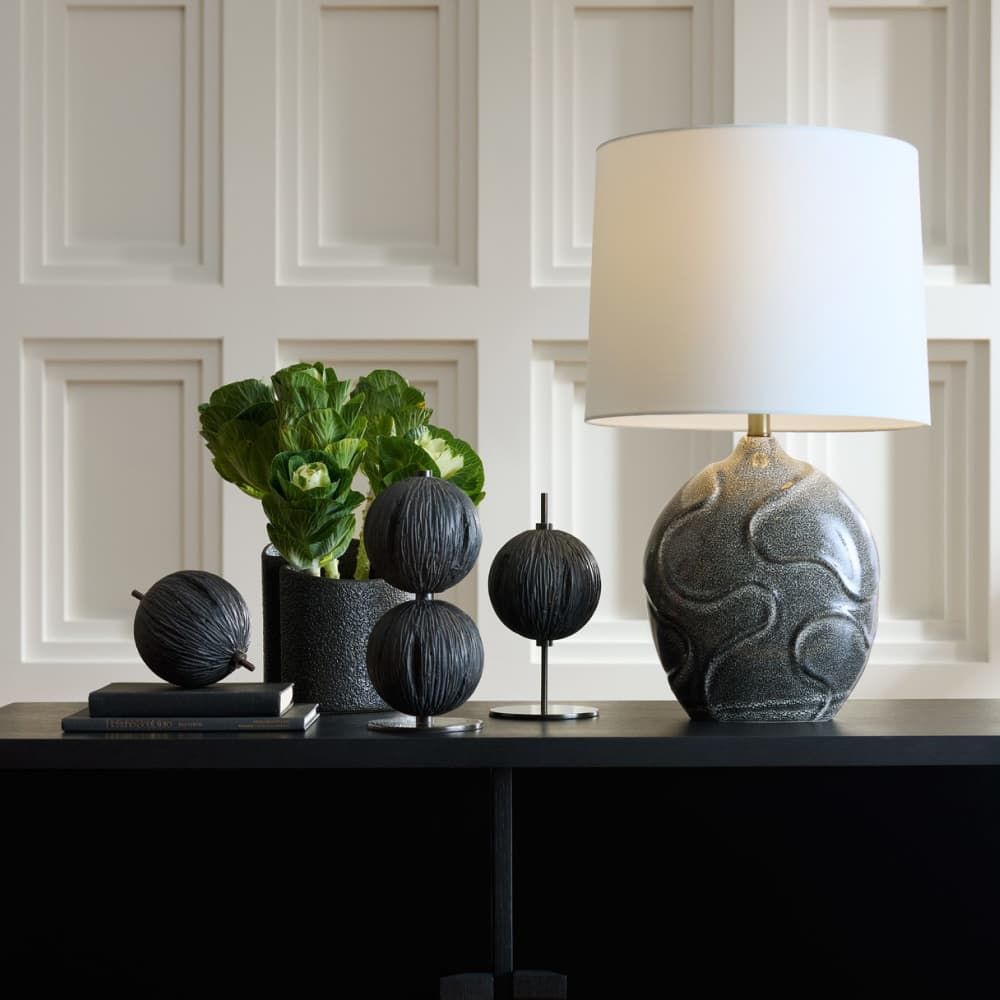 Decorative items including a lamp and plants on a table against a white paneled wall.