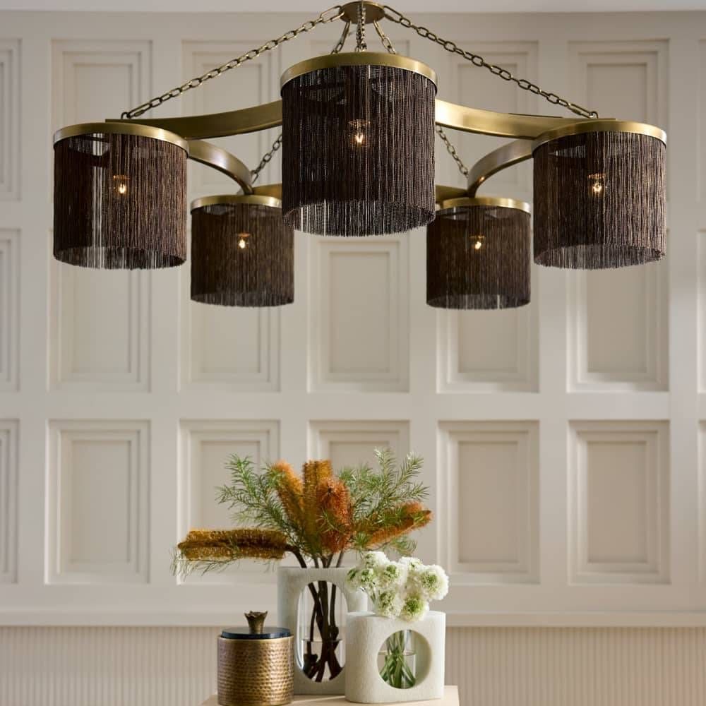 Chandelier with black lampshades and gold accents against a white paneled wall.