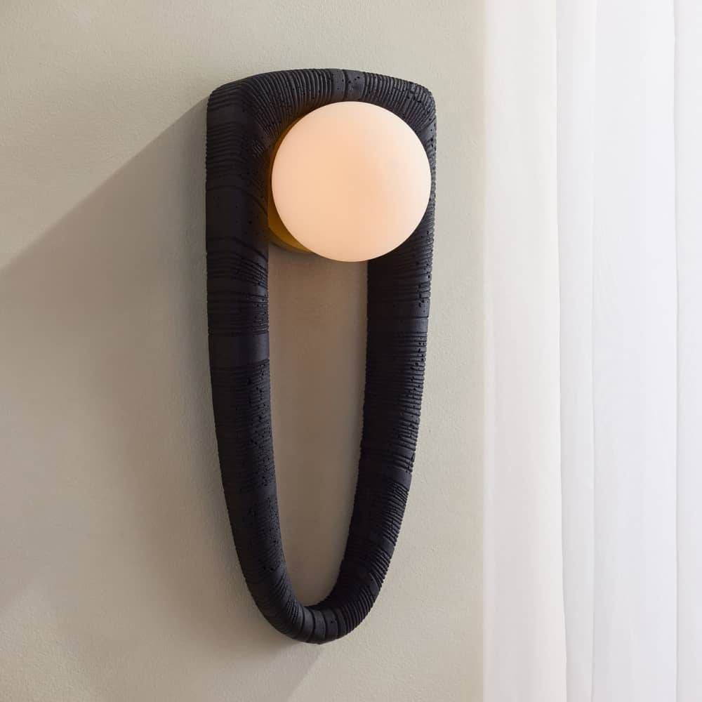 Modern wall sconce with black textured fixture and white bulb on a neutral wall.