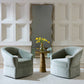 Two light blue chairs in a room with a tall mirror and a small round table with a vase of flowers.