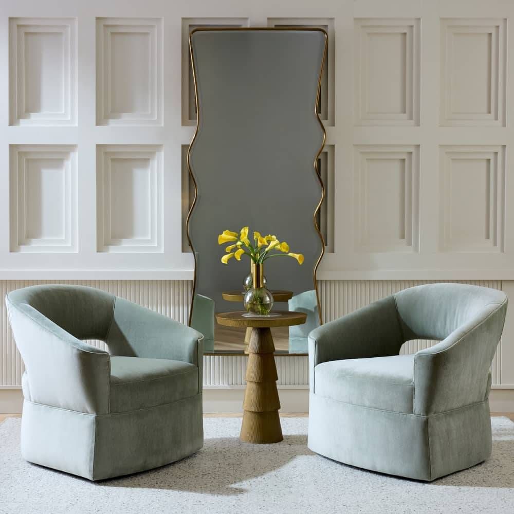 Two light blue chairs in a room with a tall mirror and a small round table with a vase of flowers.
