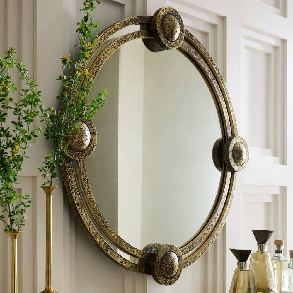 Decorative round mirror with ornate frame on a wall with plants and decor items.