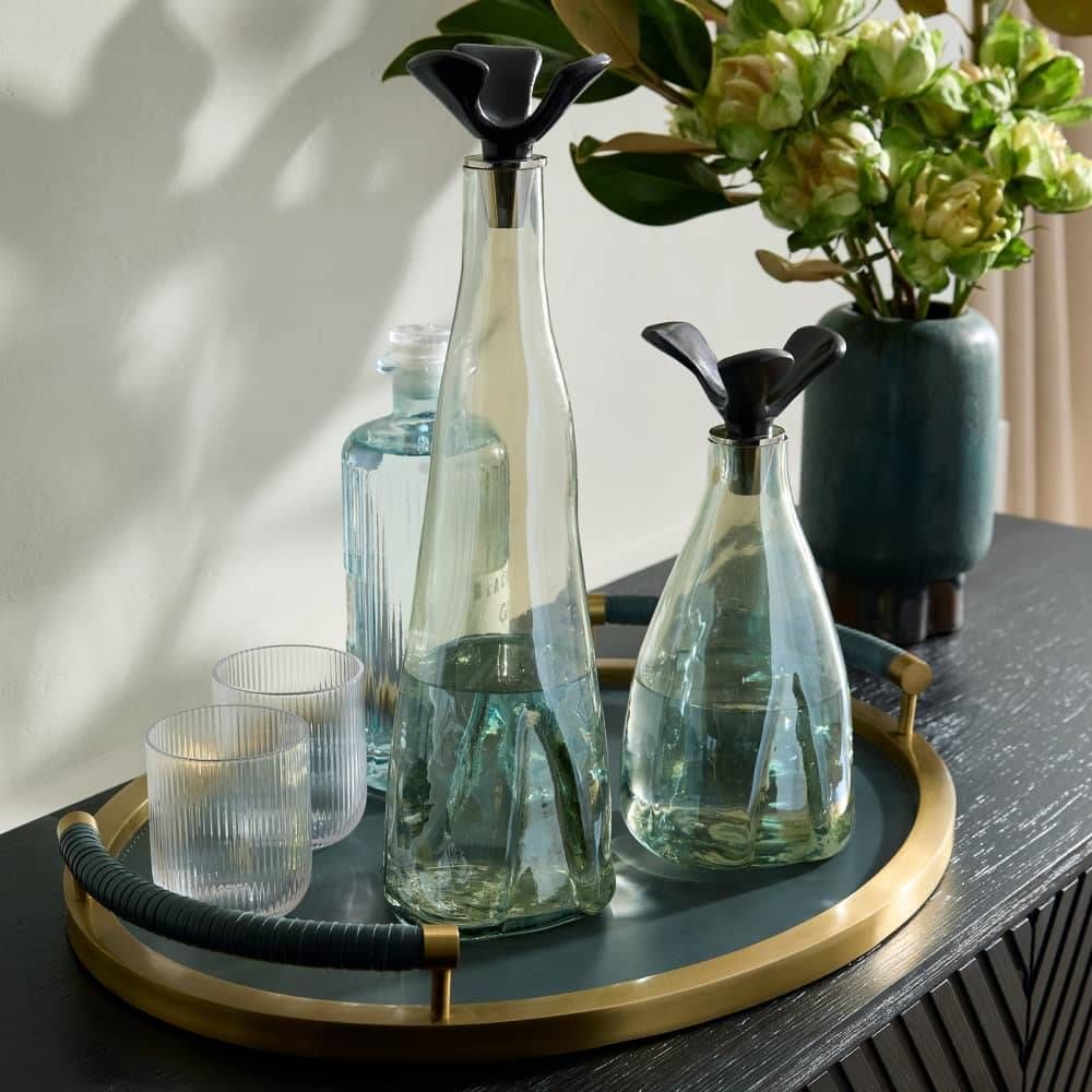 Decorative setting with glass bottles, glasses, and a vase on a tray.