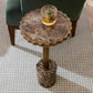 Small round marble table with a glass of whiskey on a textured floor.